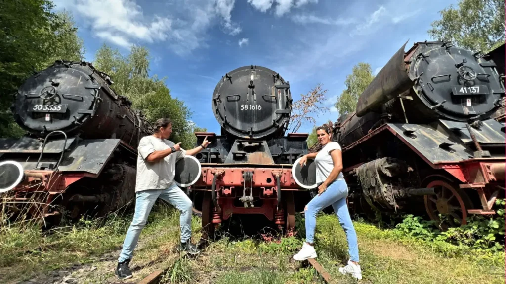 Lost Place Currywurst: Jack Silver und das Kätzchen posieren vor drei alten Dampfloks in einem verlassenen Bahngelände – Lost Place Flair trifft auf Abenteuergeist